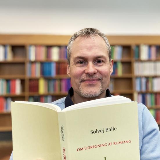 Bibliotekets litteraturformidler Anders holder Solvej Balles bog 'Om udregning af rumfang' op foran sig